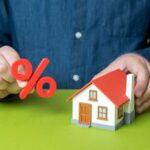 Mortgage Crisis SPIRALS — One Brutal Number Says It All Person holding a percentage symbol above a model house
