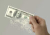 Army Budget Hole Triggers Training Axe Hand holding a disintegrating hundred dollar bill.