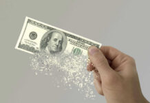 Army Budget Hole Triggers Training Axe Hand holding a disintegrating hundred dollar bill.
