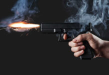 Cap, Gown… Then Deadly Gunfire A hand holding a gun with smoke and a flash from the muzzle