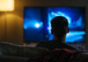 Person sitting on a couch watching a television screen in a dimly lit room