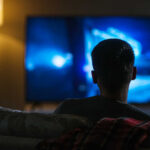 Iconic TV Dad Dies — Fans Grieve Person sitting on a couch watching a television screen in a dimly lit room