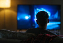 Iconic TV Dad Dies — Fans Grieve Person sitting on a couch watching a television screen in a dimly lit room