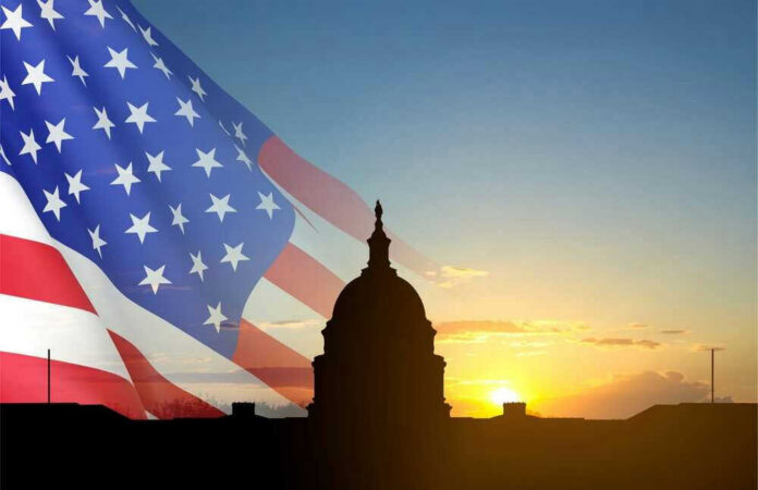 Capitol building silhouette with American flag at sunrise.