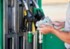 Gasoline SPIKES — Inflation SKYROCKETS Person holding cash at a gas station while preparing to refuel