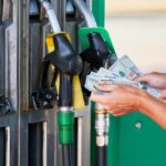 Gasoline SPIKES — Inflation SKYROCKETS Person holding cash at a gas station while preparing to refuel