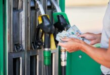 Gasoline SPIKES — Inflation SKYROCKETS Person holding cash at a gas station while preparing to refuel