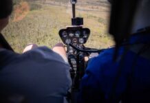 Helicopter cockpit with pilots flying over a grassy landscape
