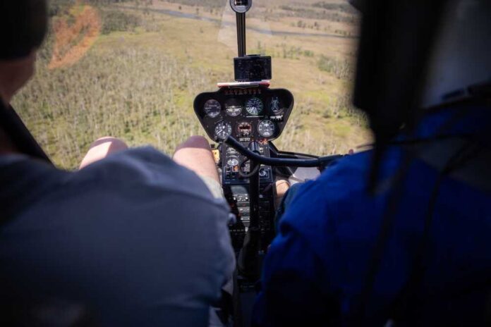 Helicopter cockpit with pilots flying over a grassy landscape