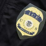 Border Hawk Tapped — Lib Panic Erupts Close-up of an ICE officer badge on a black jacket