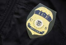 Border Hawk Tapped — Lib Panic Erupts Close-up of an ICE officer badge on a black jacket