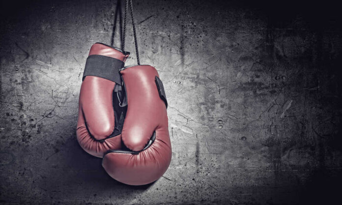 Pair,Of,Red,Boxing,Gloves,Hanging,On,Wall Red boxing gloves on a dark, textured surface.