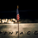 Pentagon Admits Alarming Troop Toll American flag above engraved Pentagon sign at night