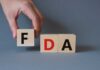 FDA’s HIGHEST Alert Hits Beloved Snack Food A hand holding a wooden block with the letter F, next to blocks spelling FDA