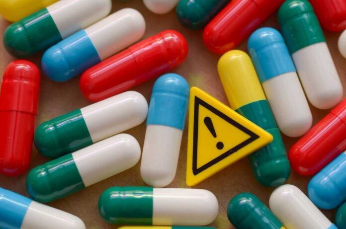 A,Pile,Of,Colorful,Medication,Capsules,Next,To,A,Caution Colorful capsules scattered around a yellow warning sign