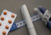 GLP-1 Results In Shocking Drop In Sick Leave?! Medication blister pack, insulin pens, and tape measure on a gray surface