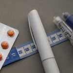GLP-1 Results In Shocking Drop In Sick Leave?! Medication blister pack, insulin pens, and tape measure on a gray surface