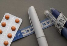 Medication blister pack, insulin pens, and tape measure on a gray surface