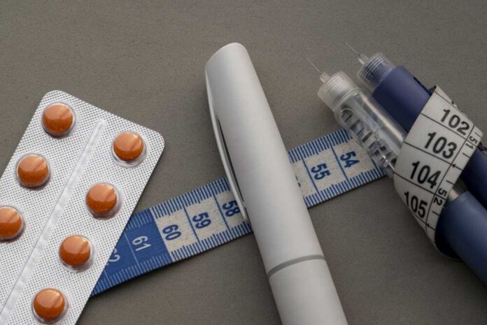 Medical,Weight,Loss,Concept,With,Insulin,Pens,,Orange,Pills,In Medication blister pack, insulin pens, and tape measure on a gray surface