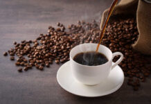 Morning Coffee Cuts Heart Risk? Spoon sprinkling instant coffee granules into a glass cup