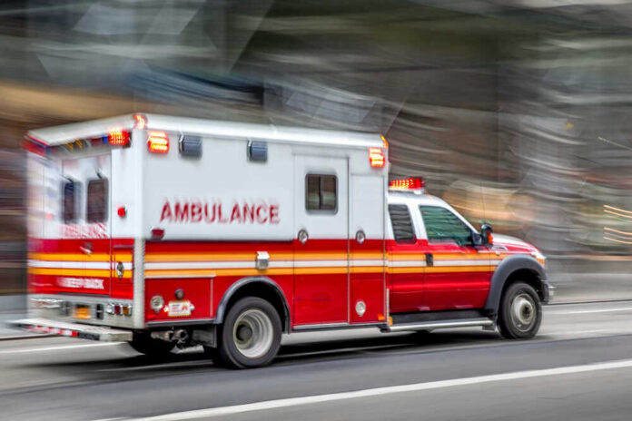 shutterstock_1495131698 Red and white ambulance driving on a city street.