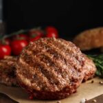 Burger Wars: Grass-Fed Gambit Announced Grilled burger patties on parchment with rosemary and tomatoes