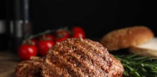 Grilled burger patties on parchment with rosemary and tomatoes
