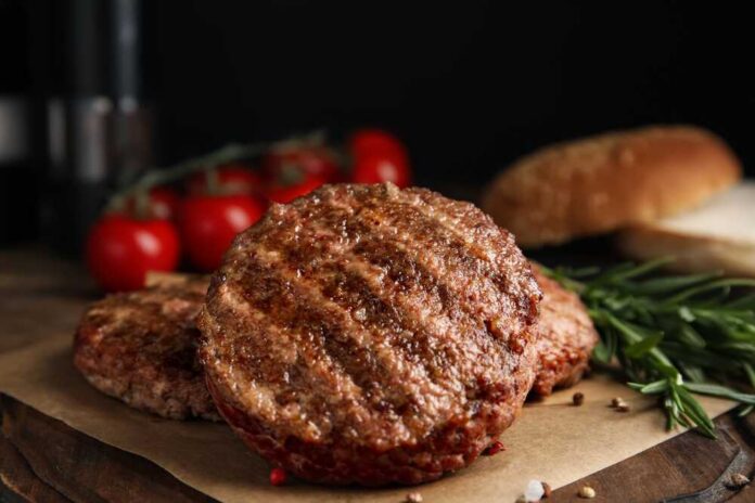 Grilled burger patties on parchment with rosemary and tomatoes