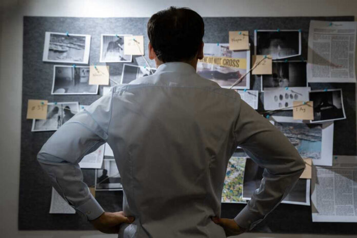 shutterstock_2140725125 Man examining investigation board with photos and notes.