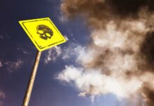 Grim Mine Find – 14 Dead Yellow warning sign with skull symbol under dramatic cloudy sky
