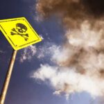 Yellow skull and crossbones warning sign against smoky sky