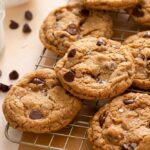 Chocolate chip cookies cooling on a wire rack beside a glass of milk