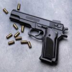 Hero Gunshots Changed Everything Black semi-automatic pistol with scattered brass cartridges on a gray surface