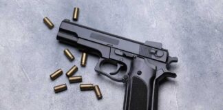 Black semi-automatic pistol with scattered brass cartridges on a gray surface