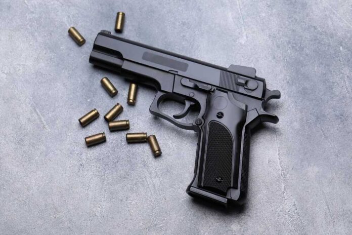 Black semi-automatic pistol with scattered brass cartridges on a gray surface