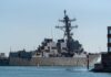 Naval destroyer sailing near a harbor with buildings in view