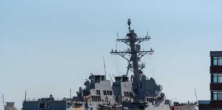 Naval destroyer sailing near a harbor with buildings in view