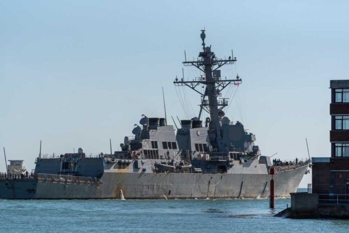 Naval destroyer sailing near a harbor with buildings in view