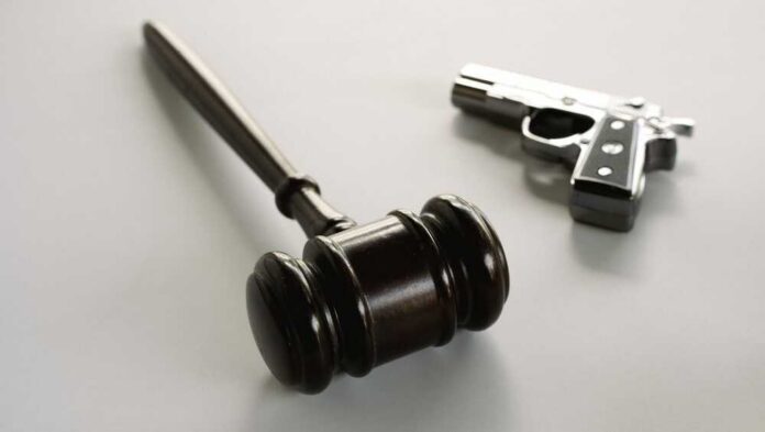 Wooden,Judge,Gavel,With,Handgun,In,Background,Depicting,Gun,Control wooden judge's gavel with a handgun in the background