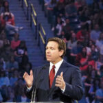 DeSantis Scores Another Crime Record-Breaker Ron DeSantis speaking at a podium before a large audience