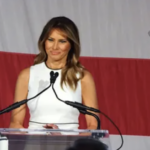 Melania Trump speaking at a podium with microphones