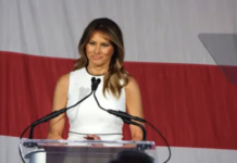 Melania Trump speaking at a podium with microphones