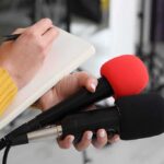 FBI Nails 40-Year Ghost — How’d He Slip By? Journalist holding two microphones while writing in a notebook