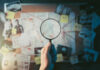 Magnifying glass over investigation board with photos and strings.