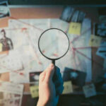 Magnifying glass over investigation board with photos and strings.