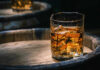 Glass of whiskey with ice on a wooden barrel.
