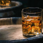 Trump’s Golf-Course Tariff Bombshell Glass of whiskey with ice on a wooden barrel.