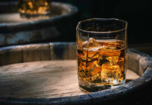 Glass of whiskey with ice on a wooden barrel.
