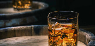 Glass of whiskey with ice on a wooden barrel.
