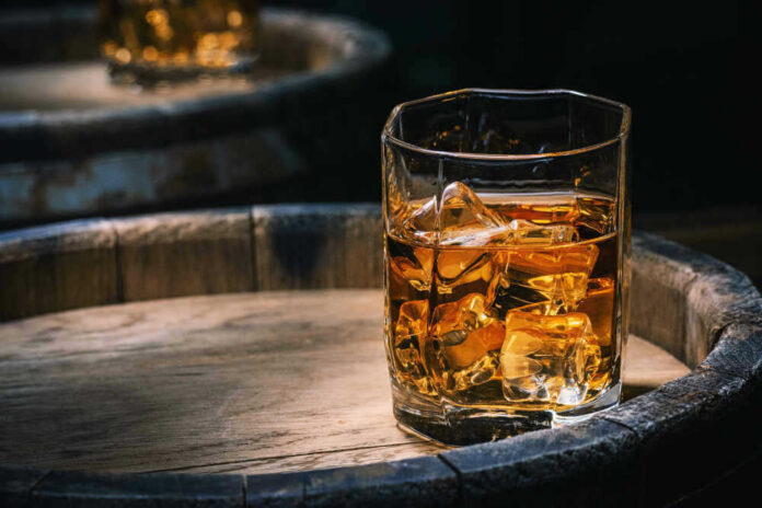Glass of whiskey with ice on a wooden barrel.